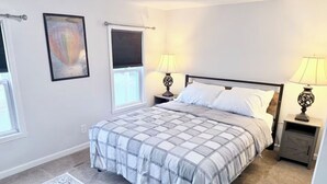 Un dormitorio con cama, dos mesitas de noche, una ventana y una alfombra.