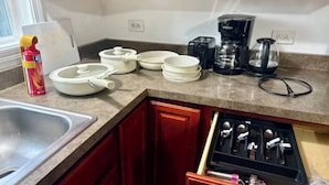 Una cocina con un lavamanos, platos blancos, cuencos, una cafetera y un cajón para utensilios.