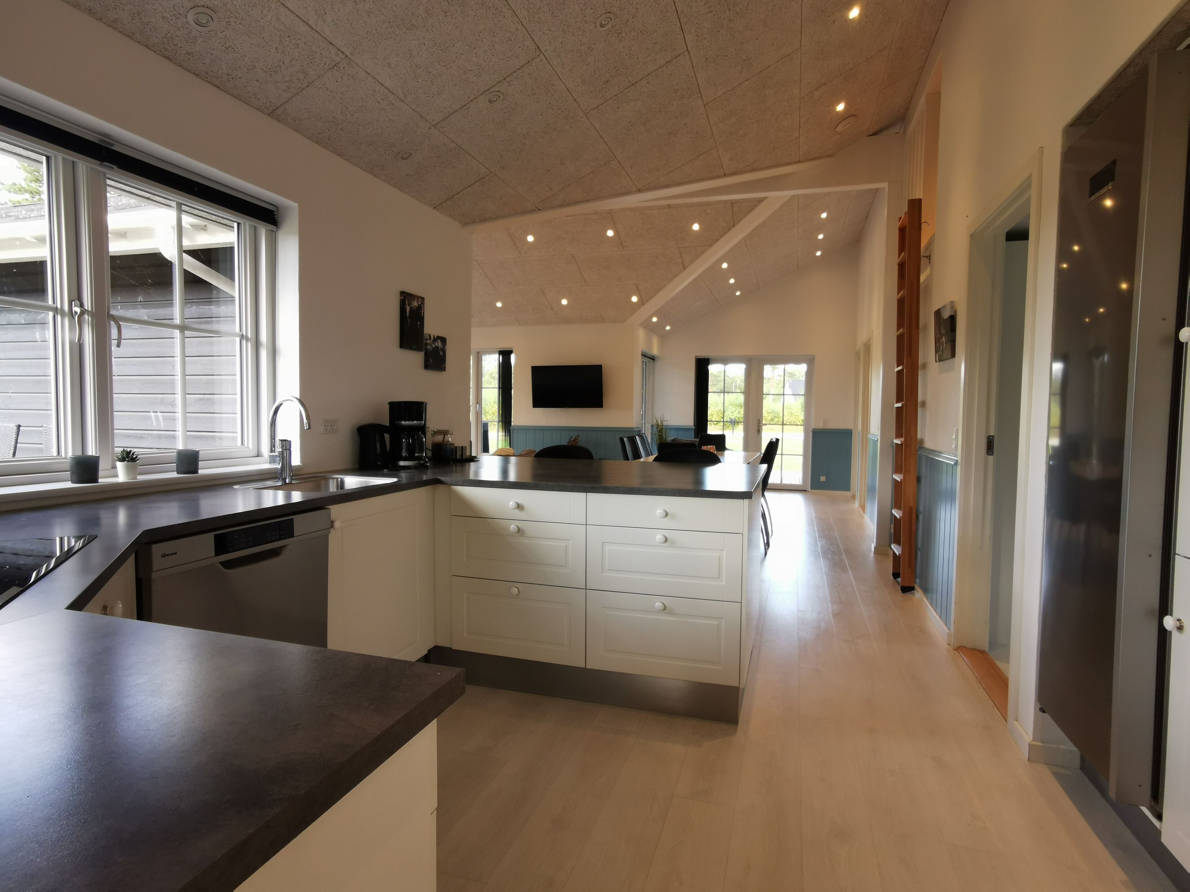Une cuisine moderne dotée d’un îlot central, de meubles blancs et d’une grande fenêtre qui laisse entrer la lumière naturelle.