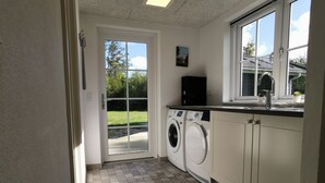 Une buanderie avec une porte donnant sur l’extérieur, un lave-linge, un évier et une fenêtre.