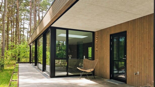 A modern building with large glass doors, a concrete pathway, and a wicker chair outside. - Modern Holiday Home on Læsø, Style, Space, and Scandinavian Charm (Læsø)