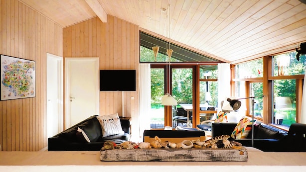 A cozy room with wooden walls, a large window, a flat-screen TV, and a wooden tray with seashells. - Charming Holiday Home With Spa and Sauna (Læsø)
