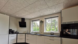 A modern kitchen with white cabinets, black countertops, and a large window providing a view of greenery outside. - Modern Holiday Home With Nature Views in Læsø (Læsø)