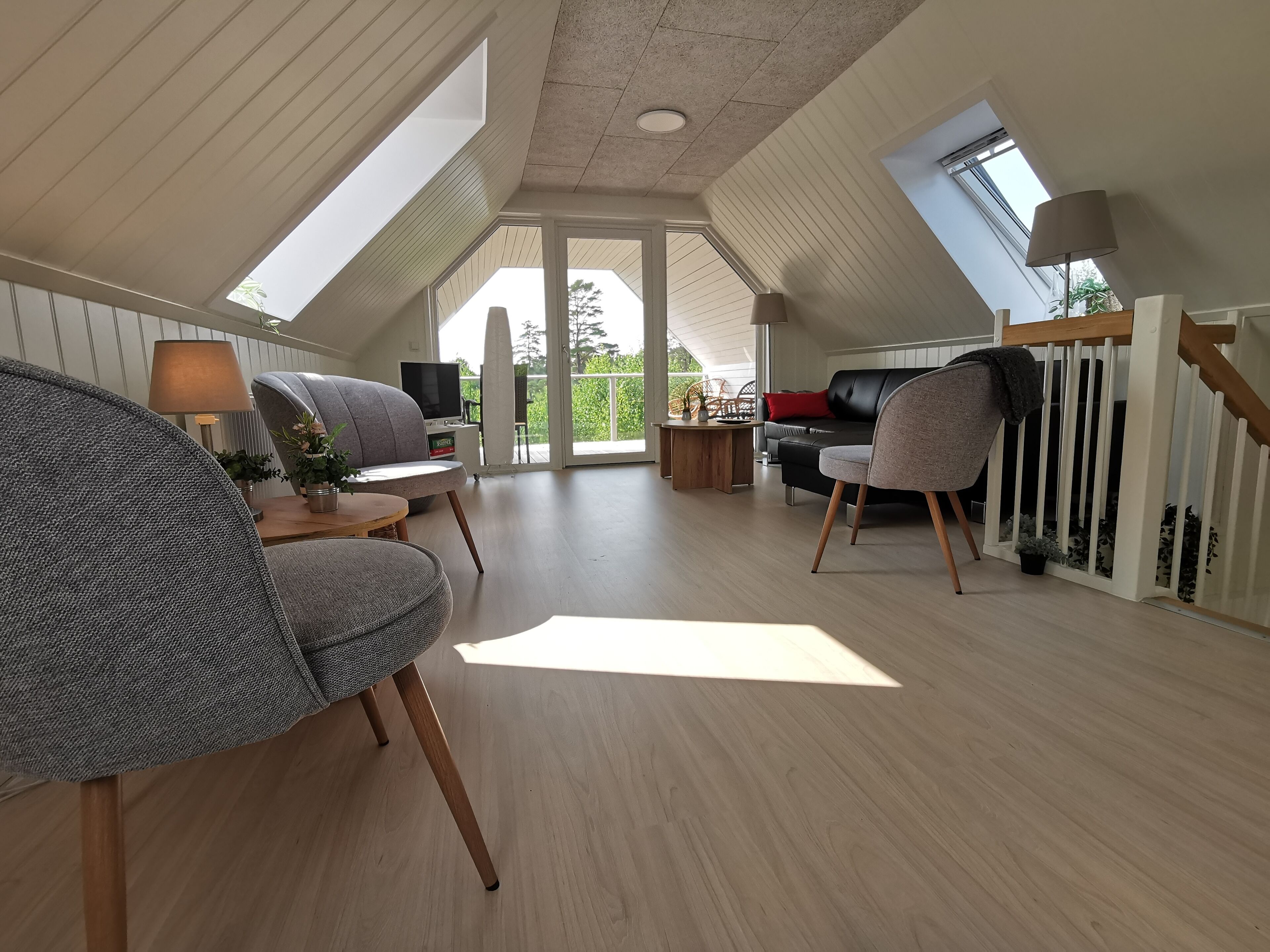Un loft espacioso con techos altos, tragaluces, un sofá de cuero negro, sillones grises, una mesa de centro de madera y un televisor.