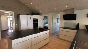 A modern kitchen with a large island, white cabinetry, and a flat-screen TV mounted on the wall. - Panoramic Views and Luxurious Comfort on Læsø Island and Sleeps up to 16 Persons (Læsø)