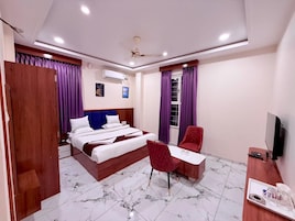 Habitación de hotel con cama, escritorio, silla, televisor y ventana con cortinas.