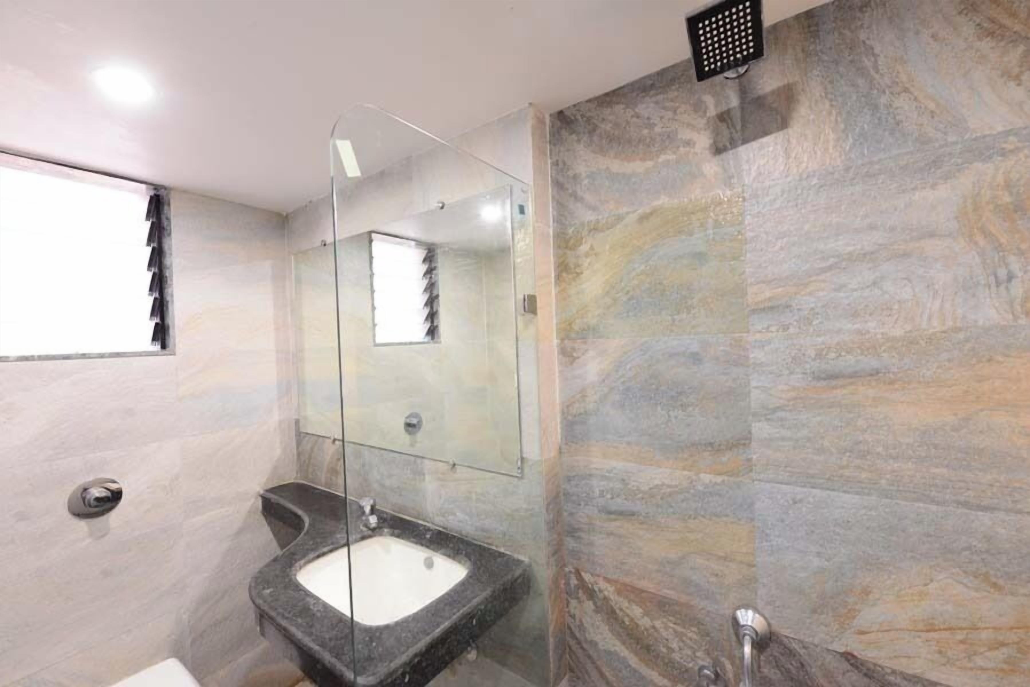 Une salle de bain moderne avec un lavabo en granit, une cabine de douche en verre et un mur en marbre.