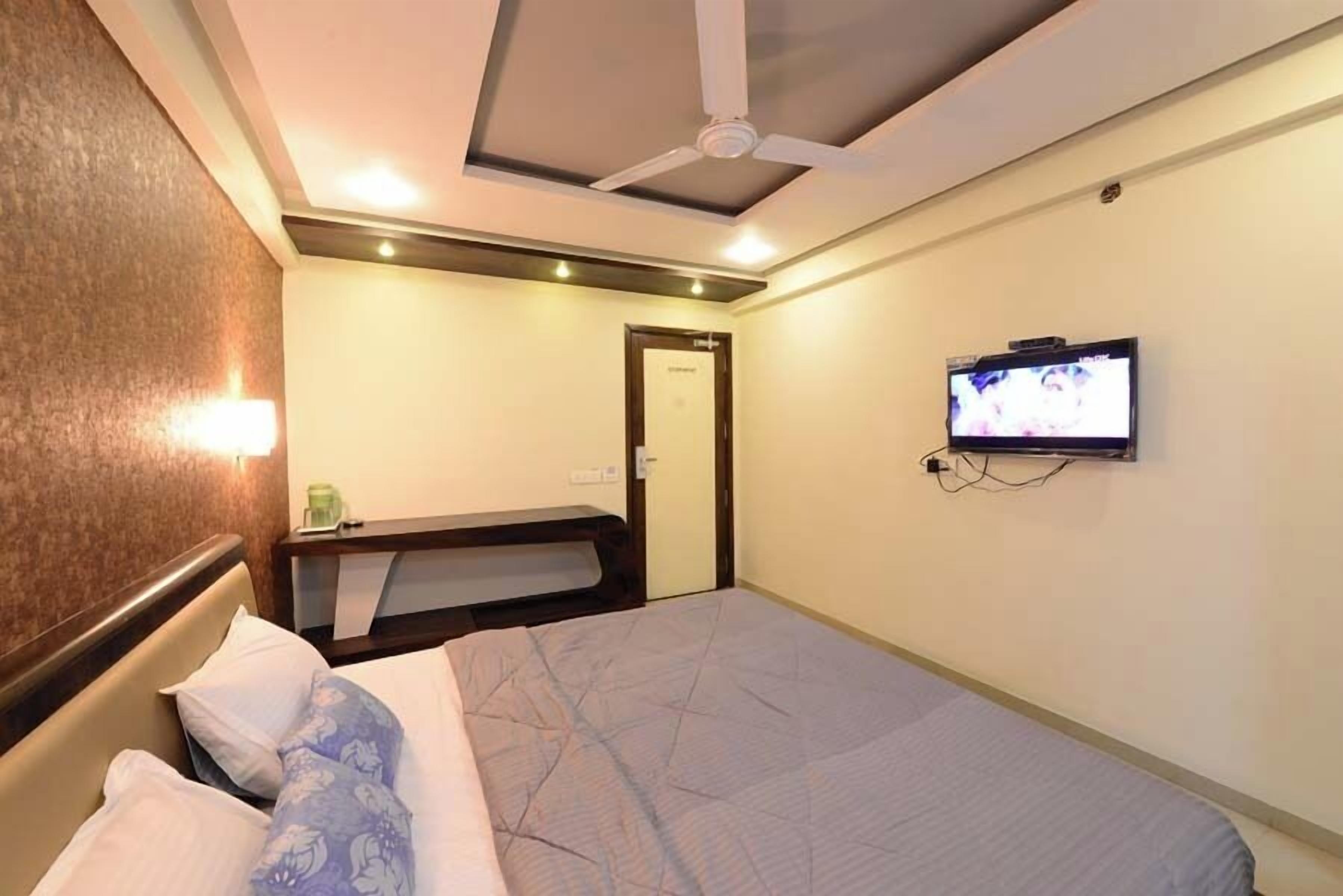 A hotel room with a bed, a television mounted on the wall, a ceiling fan, and a small table with a chair.