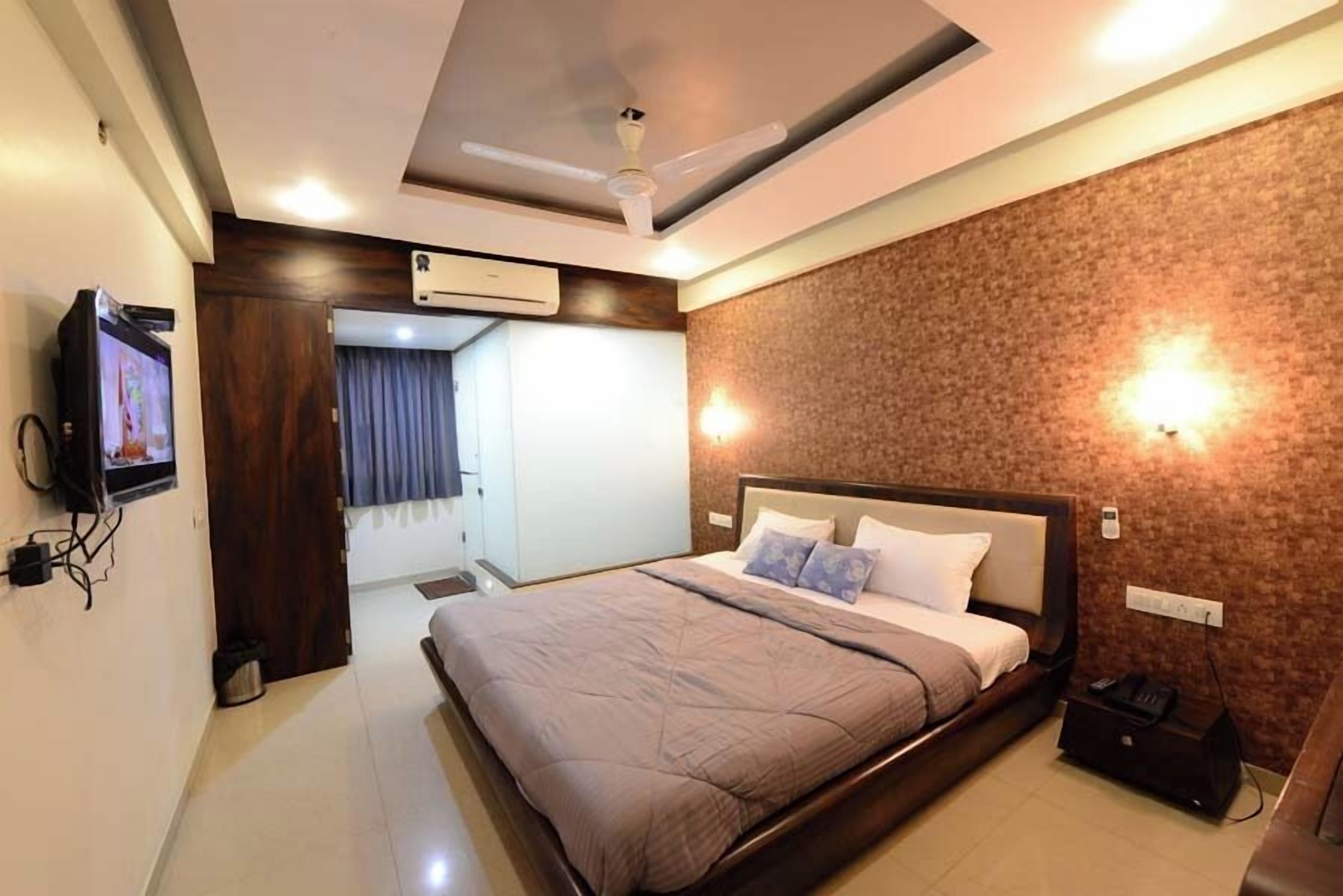 A modern hotel room with a large bed, ceiling fan, air conditioning unit, and a television on the wall.