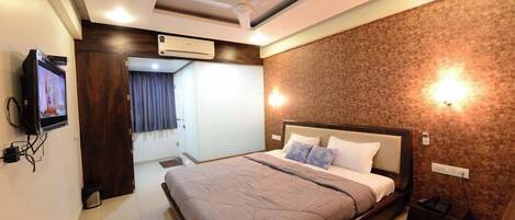 A modern hotel room with a large bed, ceiling fan, air conditioning unit, and a television on the wall.