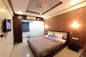 A modern hotel room with a large bed, ceiling fan, air conditioning unit, and a television on the wall. - Hotel Manila (Ahmedabad)