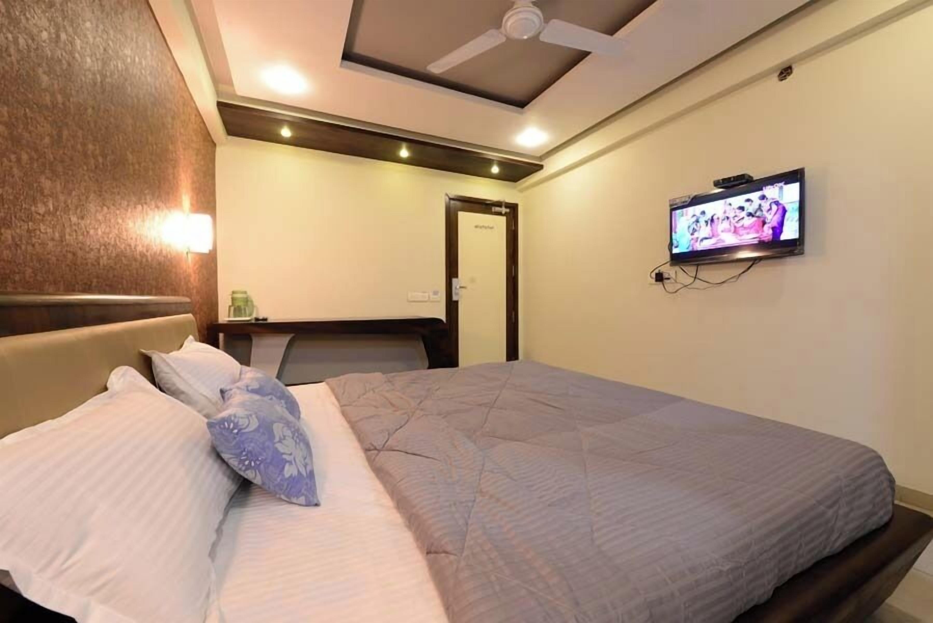 A hotel room with a bed, a television mounted on the wall, a ceiling fan, and a door.