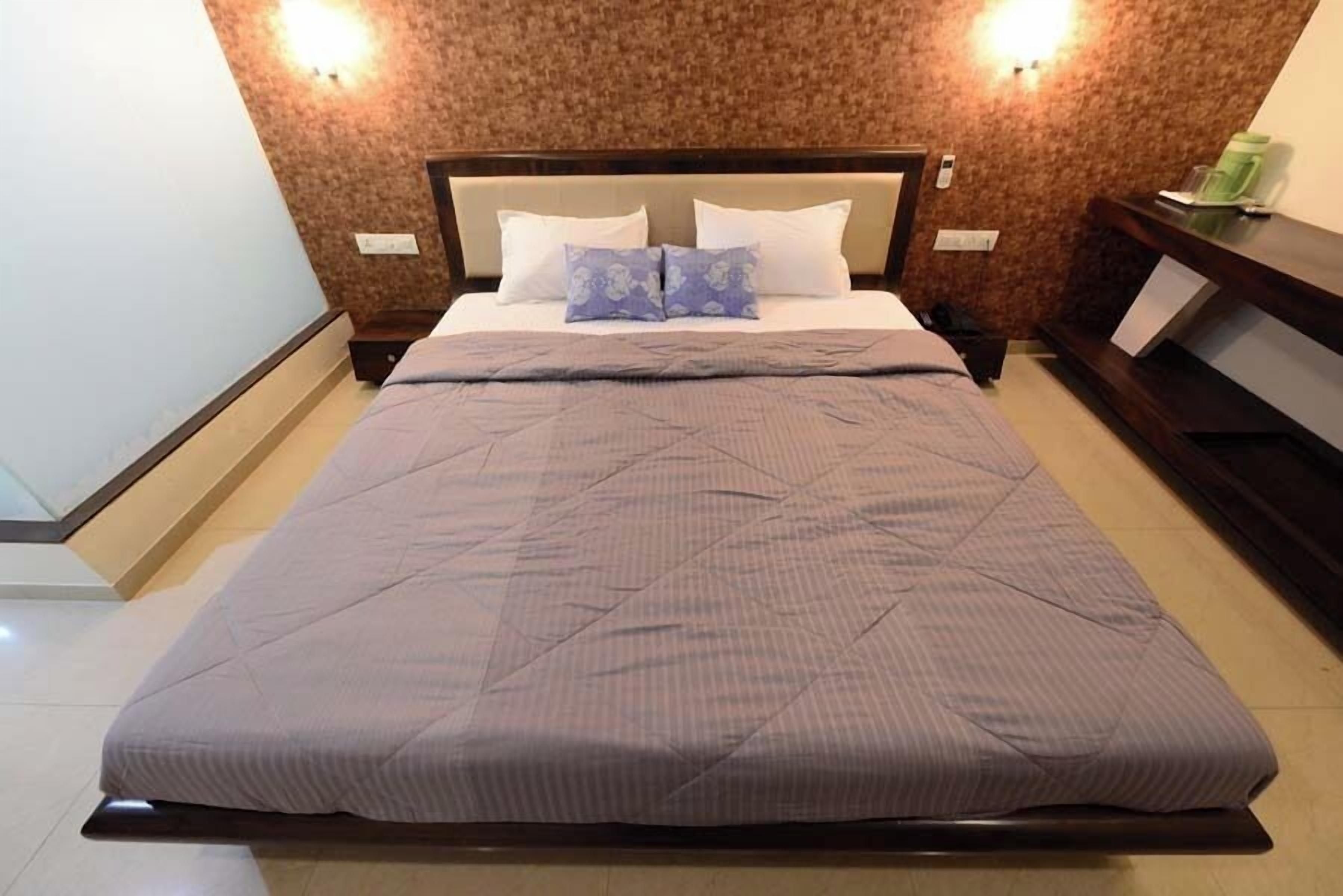 A neatly made bed with a quilted bedspread and two pillows, a wooden headboard, and a wall-mounted light fixture.