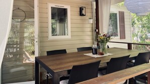 A dining area with a wooden table and chairs, a window with a view of greenery, and a hanging lantern. - Comfortable mobile home in the south of France - perfect family vacation near the beach (Vias)