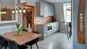 Une cuisine moderne avec des meubles blancs, une table à manger en bois et un luminaire suspendu.