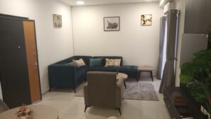 Een woonkamer met een donkerblauwe bank, een beige fauteuil, een klein rond tafeltje met een bloemenvaas, en een salontafel.