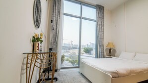 Une chambre d’hôtel avec une grande fenêtre, un lit, un bureau avec une chaise et une lampe.