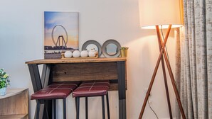 Une petite pièce accueillante, avec une table en bois, deux tabourets rouges rembourrés, une lampe sur pied et un miroir fixé au mur.