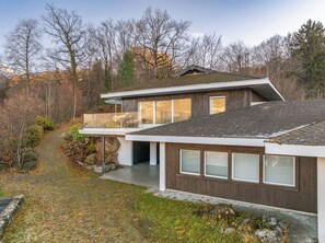 A modern two-story house with a sloped roof, large windows, and a stone pathway leading to the entrance.