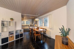 A modern kitchen with a dining area, wooden cabinets, and a large window.