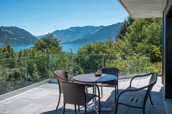 A balcony with a table and chairs, overlooking a lake and mountains.