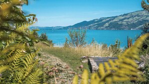 A coastal landscape with a clear view of the sea, a stone pathway, and surrounding greenery. - Lake & Mountain View Villa | 15min to Interlaken (Spiez)