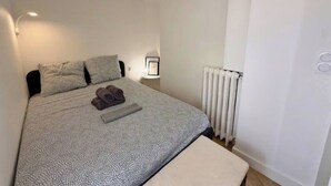 A neatly made bed with a patterned bedspread, a folded towel, and a bedside lamp. - Appartement de standing -centre- ville de Nice (Nice)