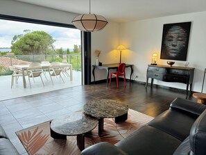A modern living room with a sofa, a coffee table, a dining area with chairs, a desk, and a lamp.