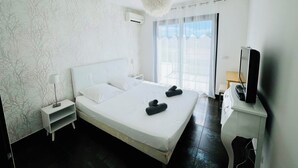 A modern hotel room with a large bed, a bedside table, a TV, and a window with curtains. - Villa Livia swimming pool, Beach 500 m, sea view (Albitreccia)