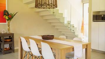 Un espace repas moderne avec une table en bois, des chaises blanches, un bol décoratif et un luminaire tressé.