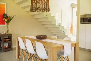 Un comedor moderno con una mesa de madera, sillas blancas, un cuenco decorativo y una lámpara de fibra trenzada.