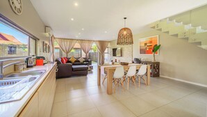 A modern kitchen with a dining area, a staircase, and a living room with a sofa and curtains. - Modern 3-Bed Home with Pool Access, Ballito (Ballito)