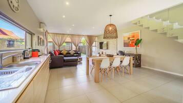 A modern kitchen with a dining area, a staircase, and a living room with a sofa and curtains.
