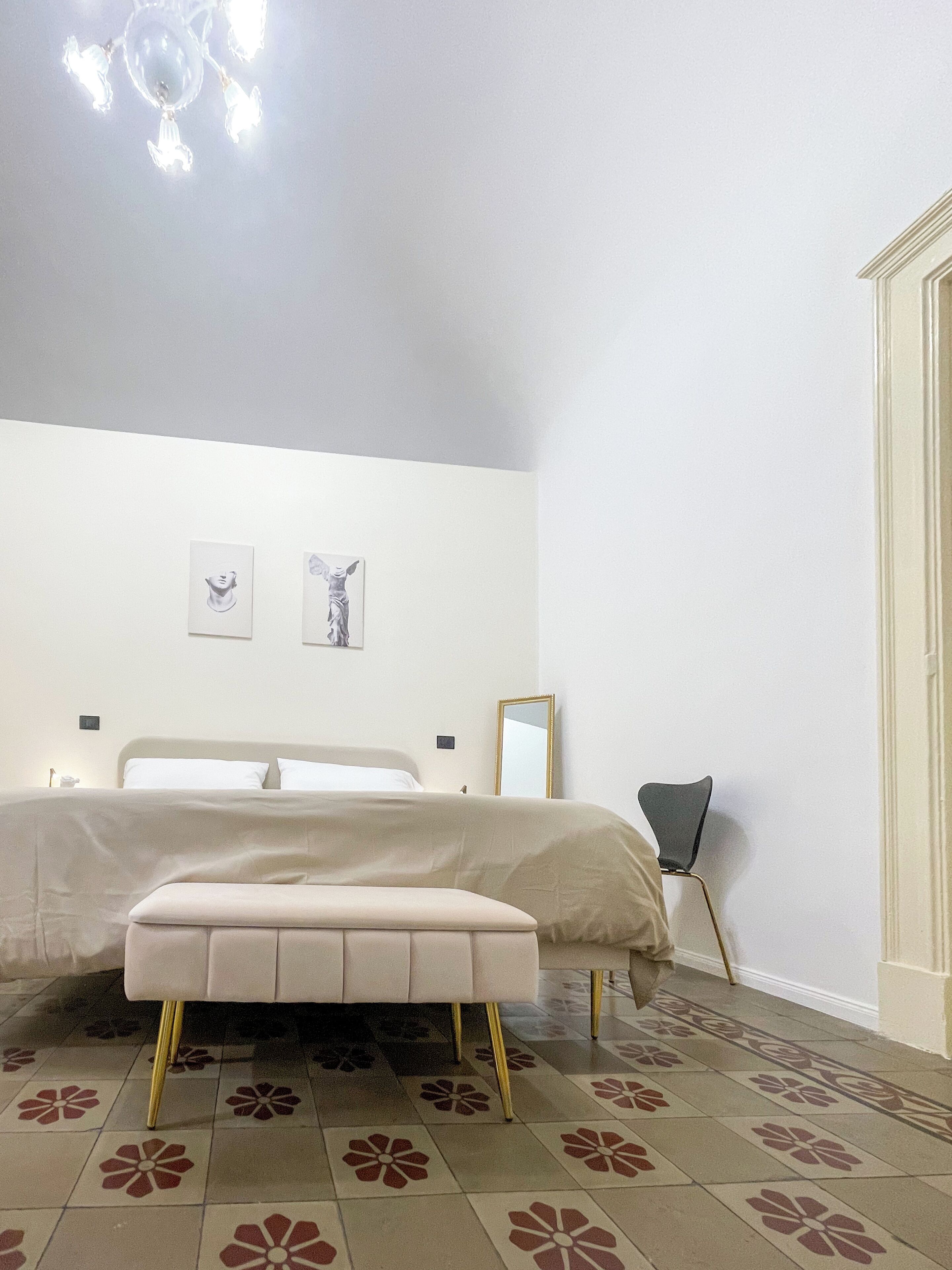 Um quarto com uma cama, um banco, uma cadeira e um espelho.