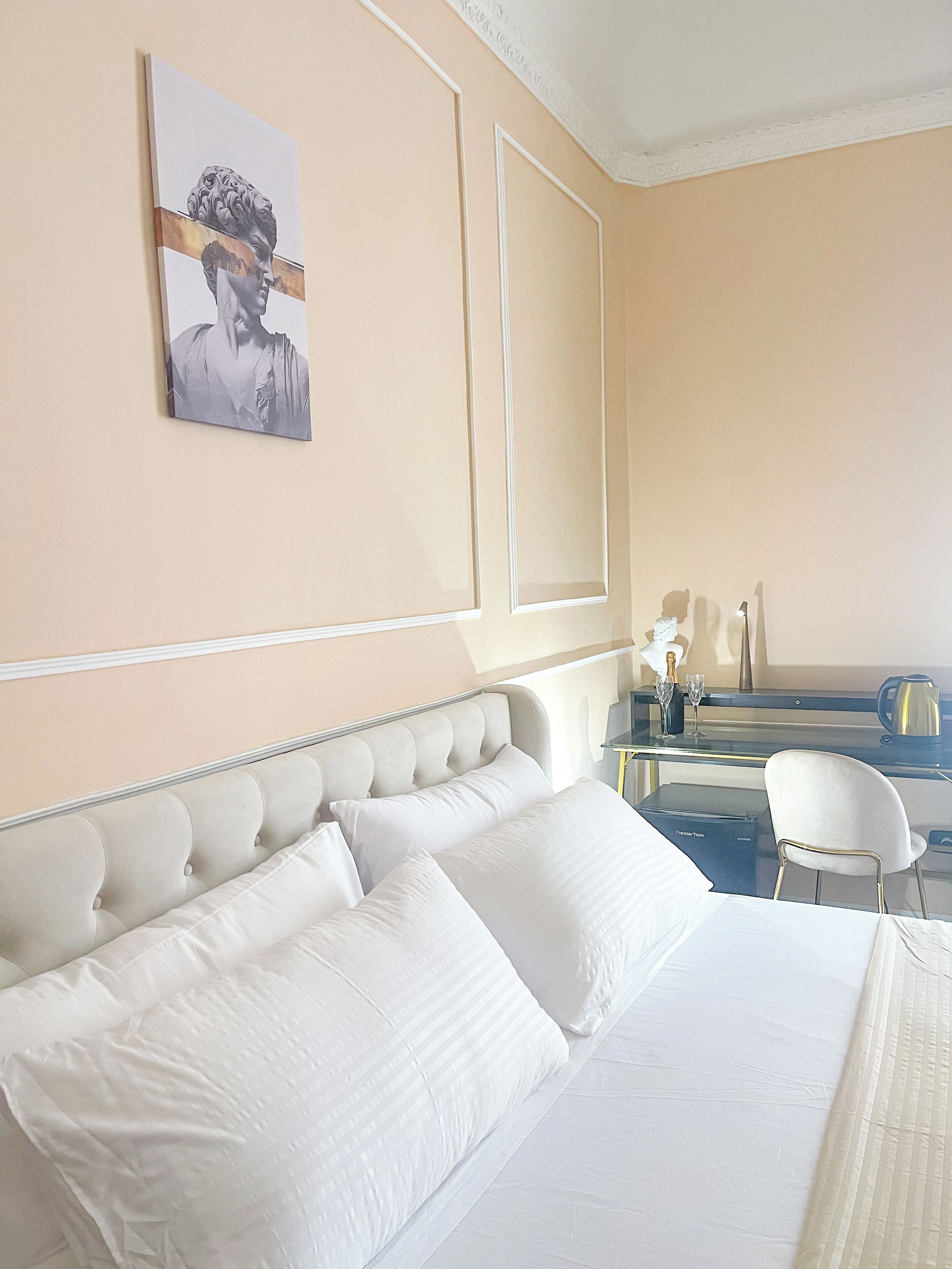 A hotel room with a large bed, a desk with a chair, a mirror, and a painting on the wall.