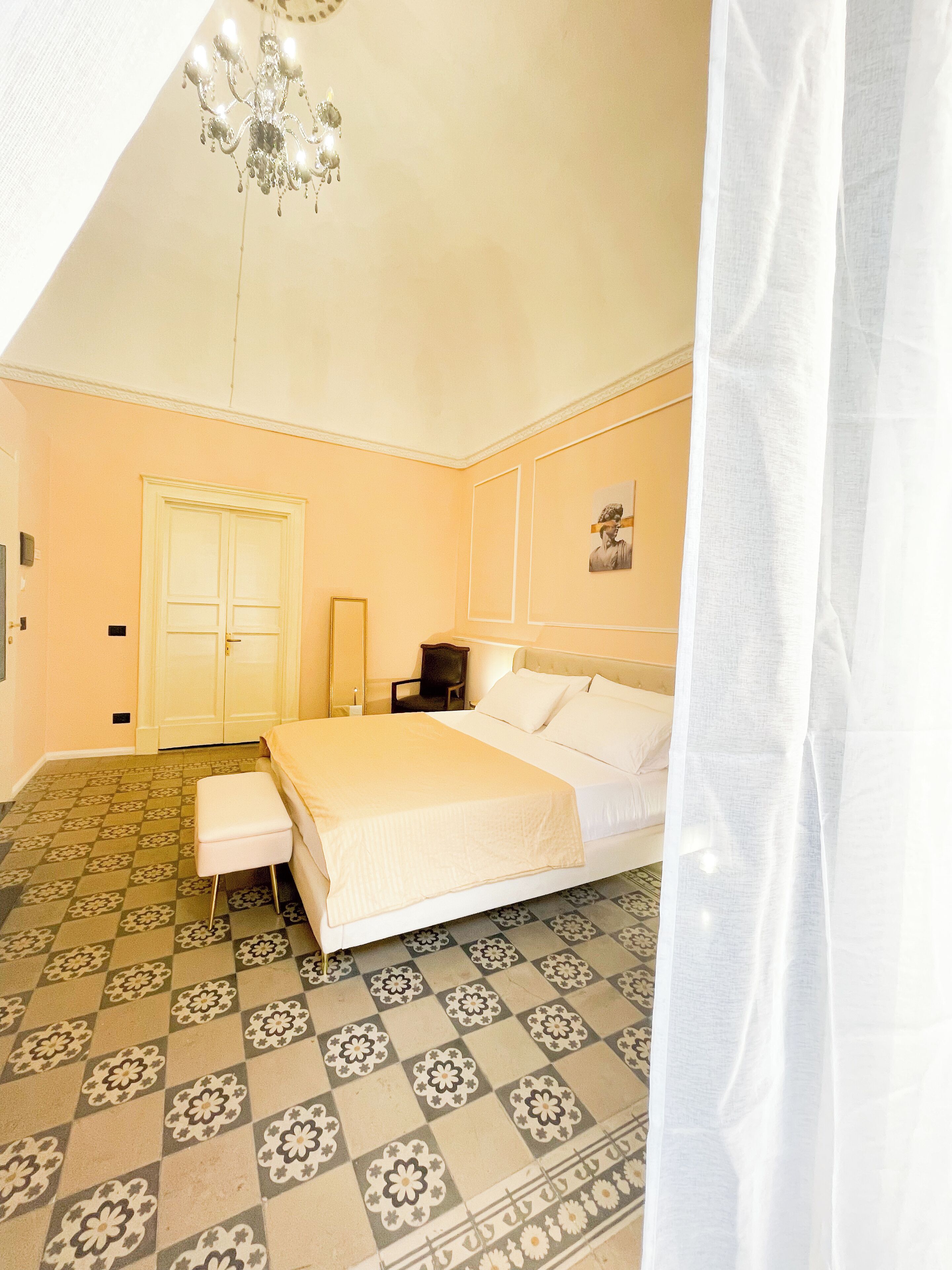 A bedroom with a bed, a nightstand, a chair, a wardrobe, and a chandelier.