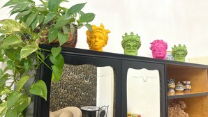 Een kamer met een bank, een tafeltje, een potplant en decoratieve objecten op planken.