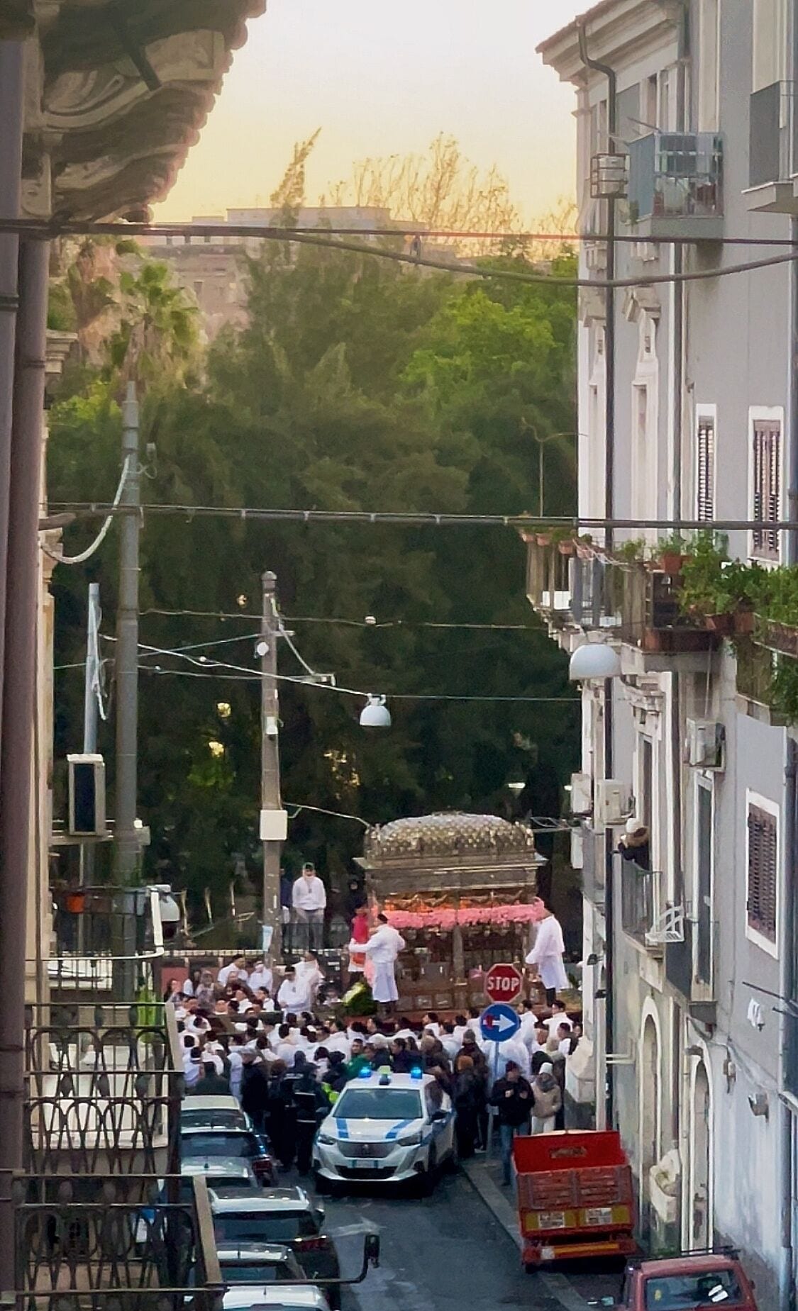 Una calle estrecha flanqueada por edificios, con una multitud de personas y un coche de policía.
