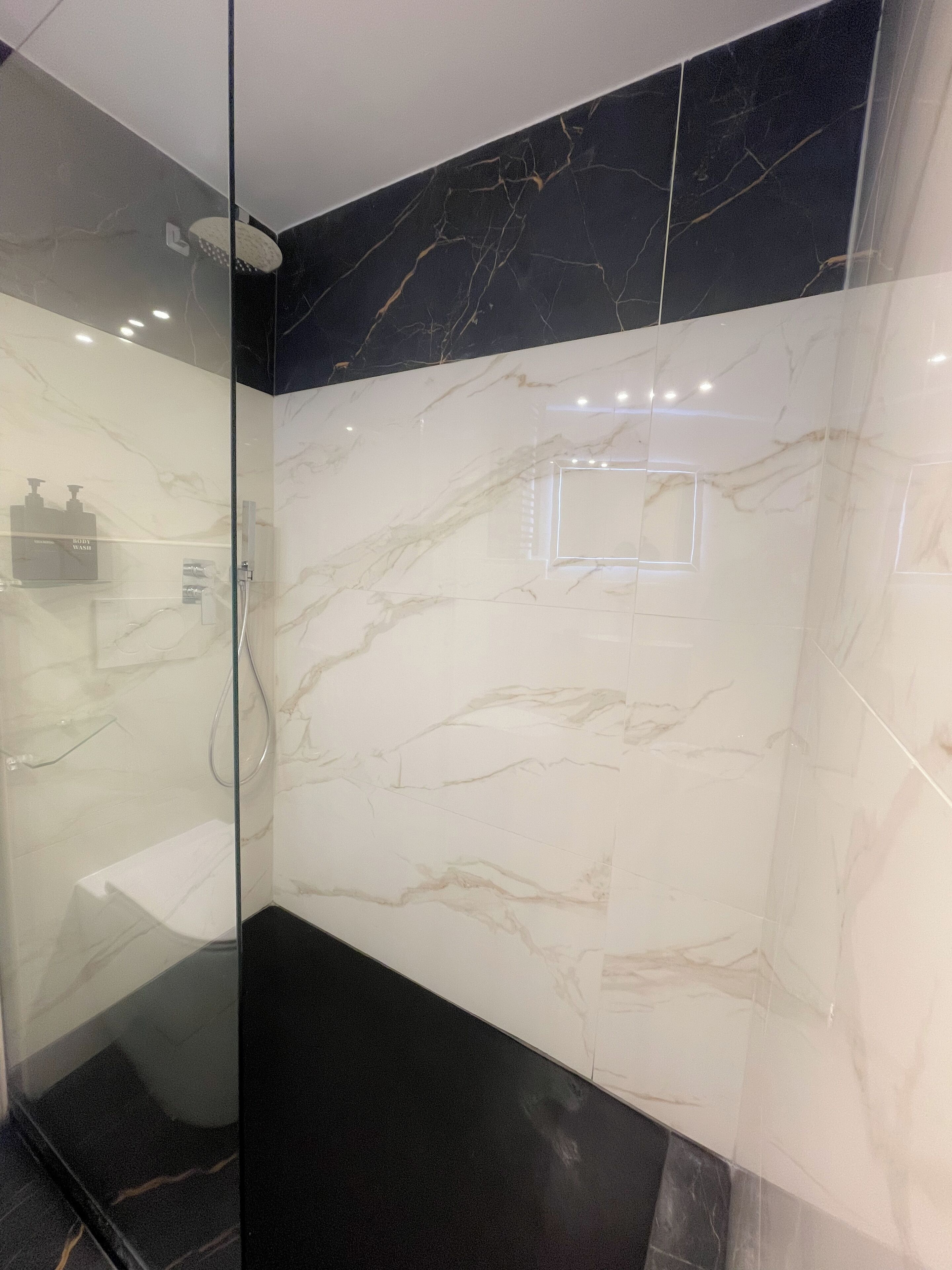 A modern bathroom with a glass shower enclosure, marble walls, and a black floor.