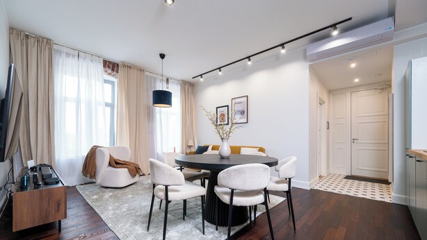 Un espace de salle à manger moderne avec une table ronde, des chaises blanches et un système d’éclairage au plafond à spots, de couleur sombre.