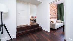 Un couloir avec un plancher en bois foncé, une porte blanche et un rideau vert.