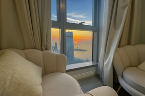 Una stanza con due poltrone beige rivolte verso una grande finestra con vista su un paesaggio urbano al tramonto.