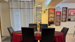 Zona pranzo con tavolo apparecchiato per quattro, circondata da sedie, un tappeto decorato e una parete con mensole.