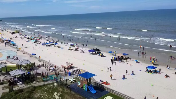 Una spiaggia con ombrelloni, un'area giochi e un molo sullo sfondo.