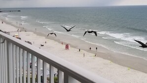Vista sulla spiaggia dal balcone, con ringhiera, l'oceano e persone che camminano sulla sabbia.