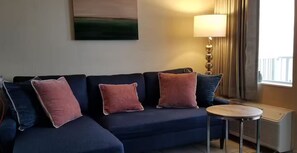 Ein dunkelblaues Sofa mit vier Kissen, ein kleiner runder Tisch, eine Lampe und eine Heizung.