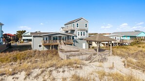 Una propiedad frente a la playa con una casa de dos pisos, un porche cubierto y una zona de playa arenosa.