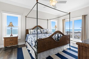 A four-poster bed with a view of the ocean, a wicker side table, and a ceiling fan. - Wishlist: Oceanfront Event Friendly Home with Elevator (Oak Island)