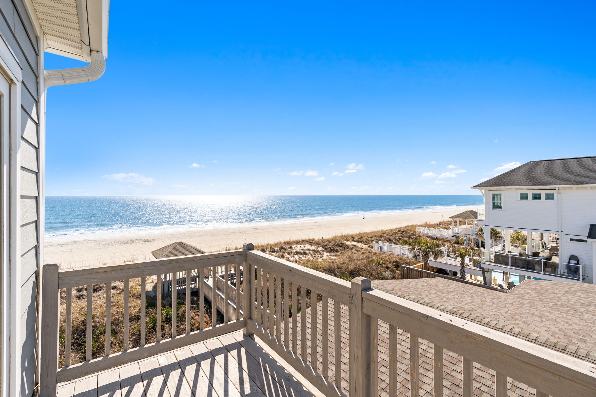 A beachfront property with a wooden deck, a view of the beach, and a white building with multiple windows.