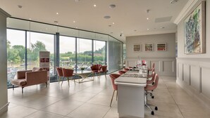 Un salón de conferencias moderno con una larga mesa, sillas rosadas y ventanas amplias que ofrecen vistas al exterior.